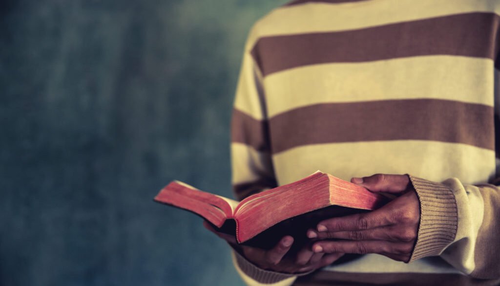 a man standing while reading bible or book over concrete wall wi