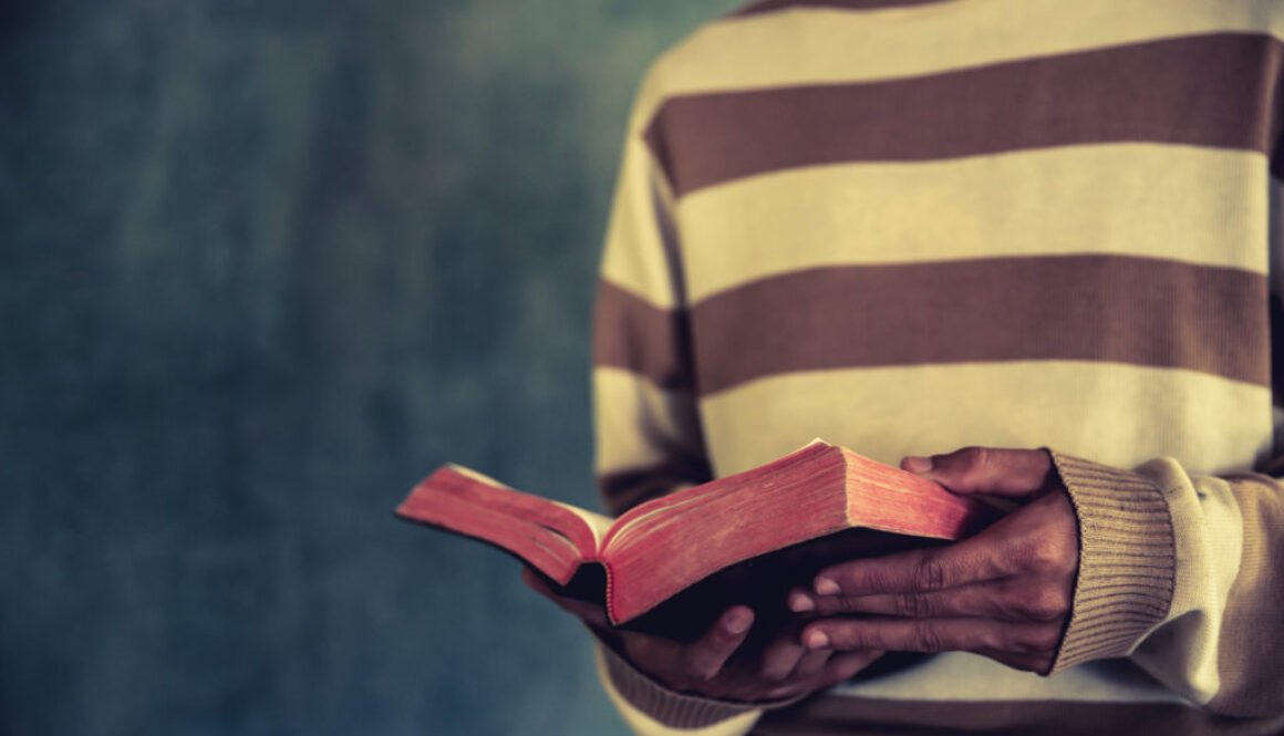 a man standing while reading bible or book over concrete wall wi