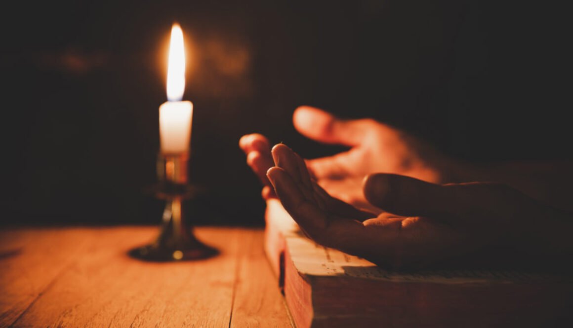 Close up man's hand is praying in the Church with lit candle, re