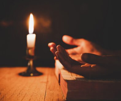 Close up man's hand is praying in the Church with lit candle, re