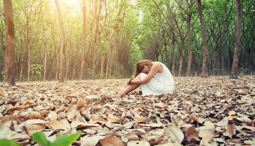 Young asian woman sadly sitting on dry leaf in the forest alone