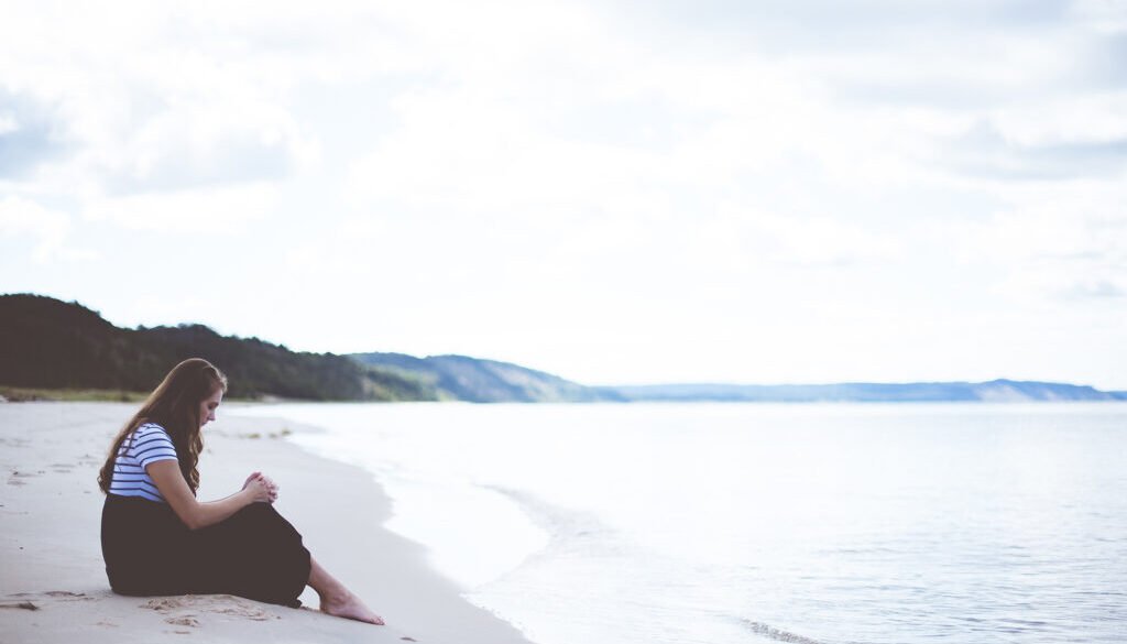 Female sitting on the beach shore with her hands on her knees while praying
