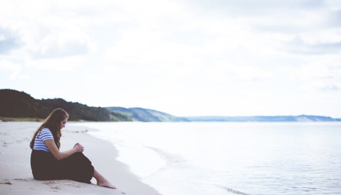 Female sitting on the beach shore with her hands on her knees while praying