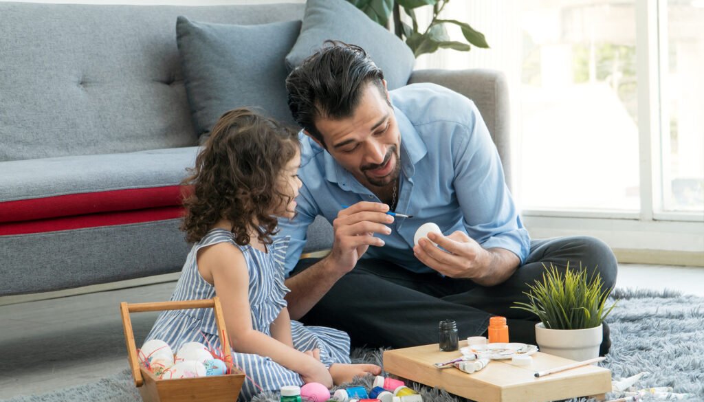 Happy family smiling. Little daughter and father painting colourful Easter eggs.