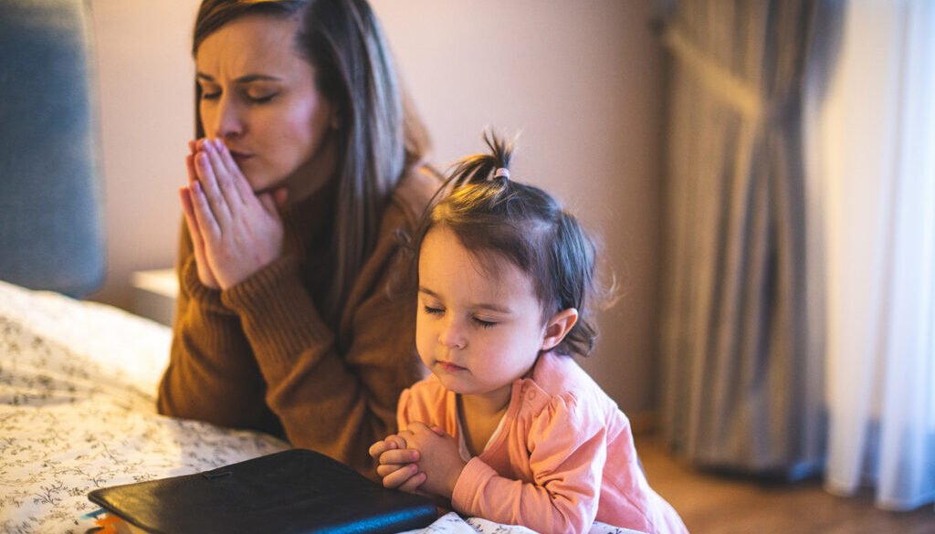 Mother and her daughter reading from bible and praying in their