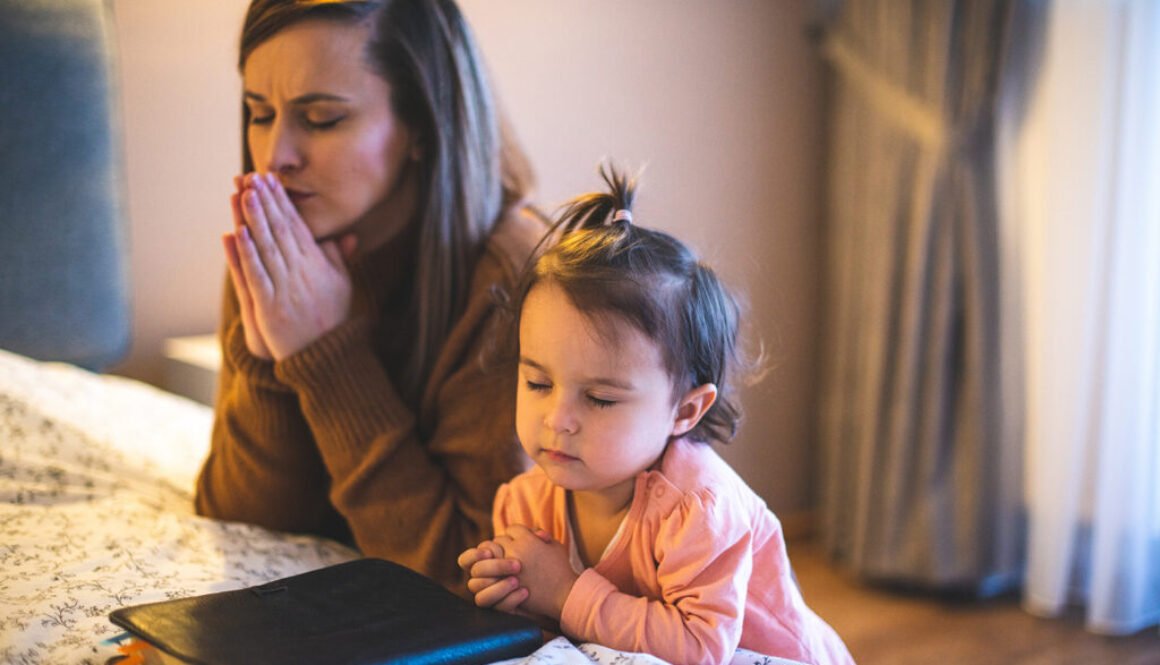 Mother and her daughter reading from bible and praying in their